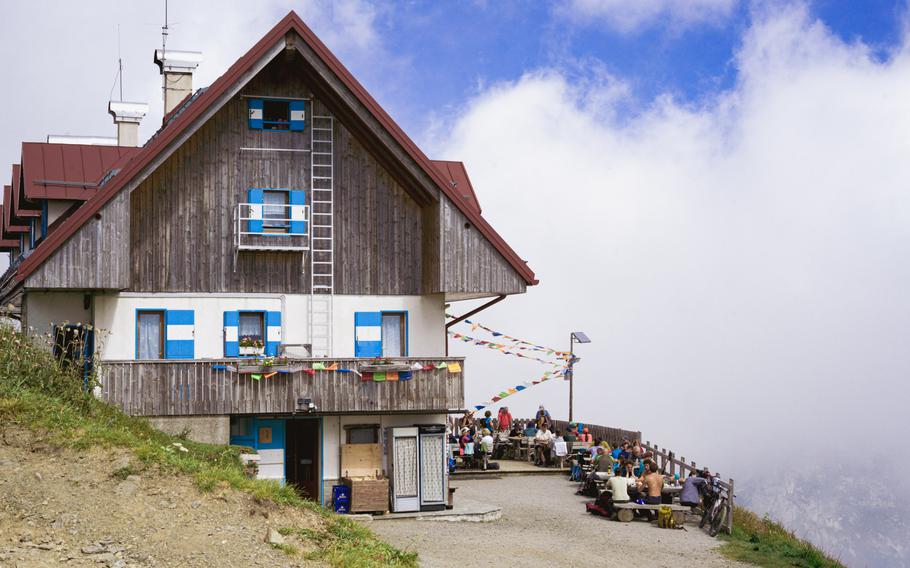 Rifugio Marianella against the view of the mountains and white fluffy clouds in the blue sky.
